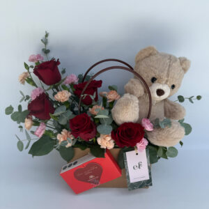 Arreglo floral romántico con rosas, mini claveles, oso de peluche y bombones en base tipo cartera